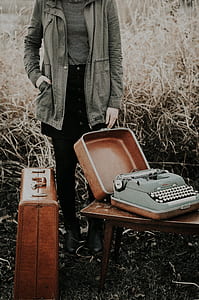 person wearing gray jacket holding brown wooden suit case with typewriter