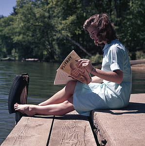 woman sitting on dock holding Playboy magazine