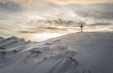 black cross on top of mountain covered snow at daytime
