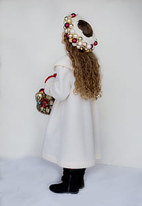 girl with brown curly hair wearing white gown carrying basket full of bauble