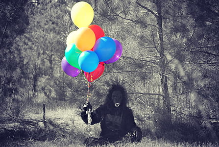 person in black gorilla costume holding balloons in forest