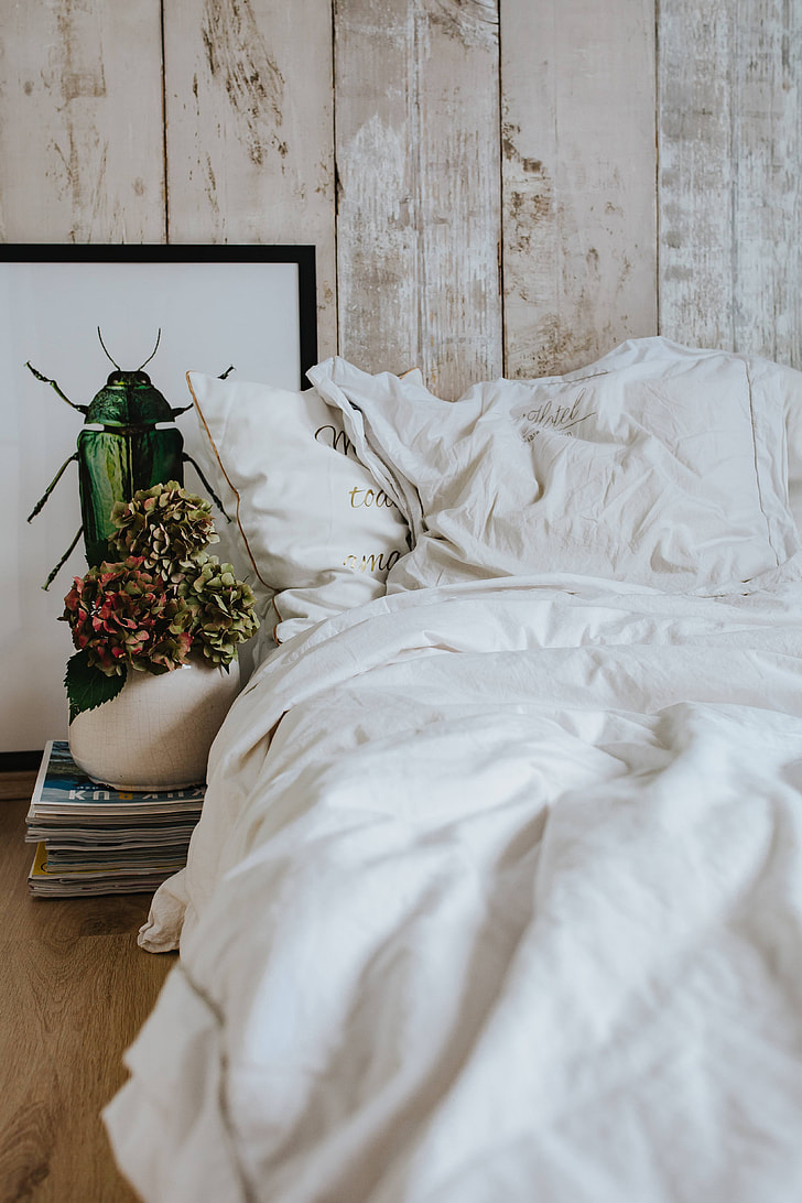 White bed sheets with a picture of a green beetle and a pot plant on a stack of magazines