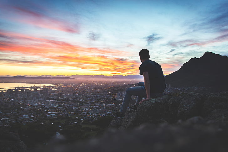 man sitting on hill with cityscape view
