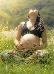 pregnant woman in black sports bra meditating during daytime