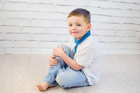 boy in white and blue polka-dots polo shirt and blue jeans sitting on brown wooden floor