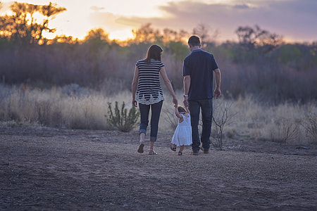man, woman, and toddler walking near grasses during golden hour