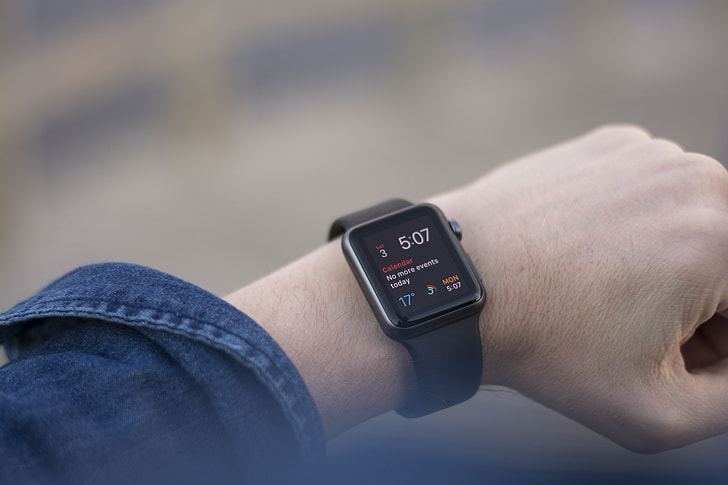person wearing space gray case black sport band Apple Watch at 5:07