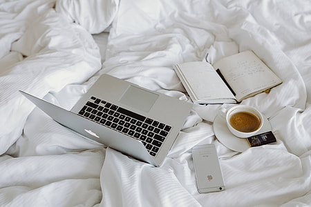 Woman working on a laptop while enjoying a breakfast coffee and chocolate in bed