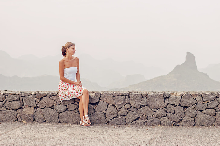 woman in white sleeveless dress sitting in stone bench