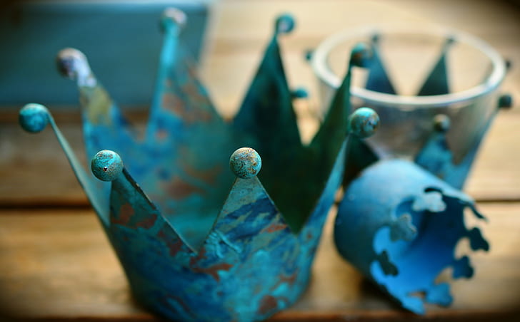 selective focus photo of three teal metal crowns on brown wooden surface