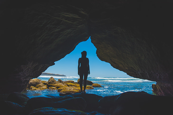 silhouette of woman standing on rock beside ocean