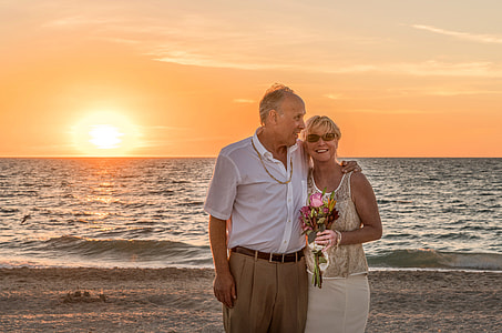 man wearing white dress shirt with woman wearing yellow floral tank top standing on shoreline during golden hour