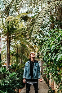 man wearing denim jacket looking up and standing on pathway between plants