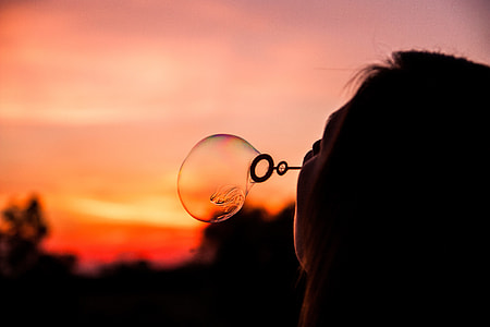 silhouette of woman blowing soap bubble during sunset