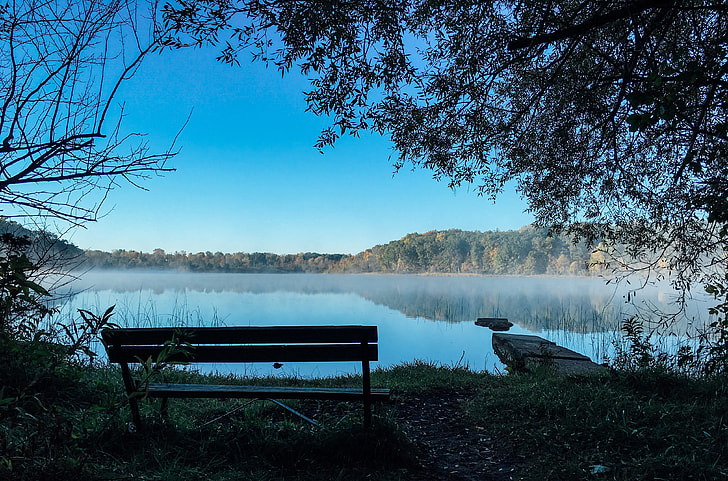 photo of bench near a lake under blue sky