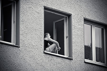 grayscale photo of woman standing beside window