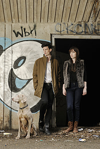 man and woman beside a weimaraner dog behind a wall