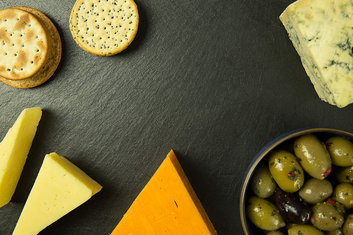 Overhead shot of cheese, olives and biscuits on a slate board
