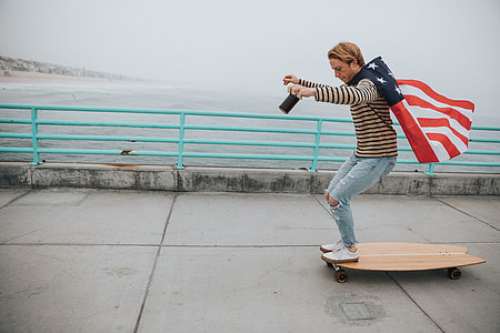 man in brown sweater holding america flag on brown longboard during daytime