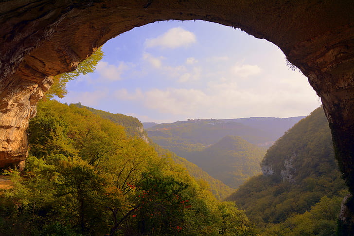 cave near green mountains under cloudy sky