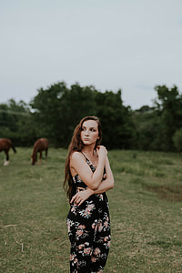 woman wearing black and red floral sleeveless jumpsuit standing on green grass field