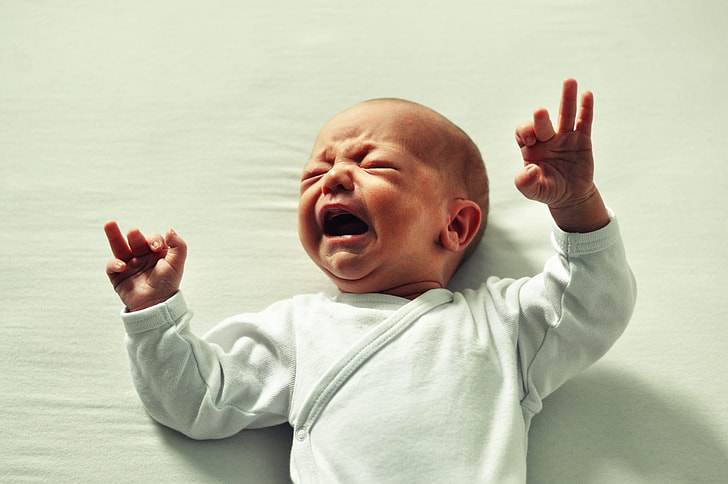 baby wearing white long-sleeved shirt crying
