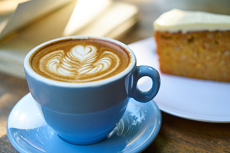 close-up photo of cappuccino in blue ceramic mug and saucer beside cake