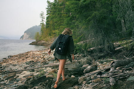 person wearing green dress shirt walking on rocky seashore