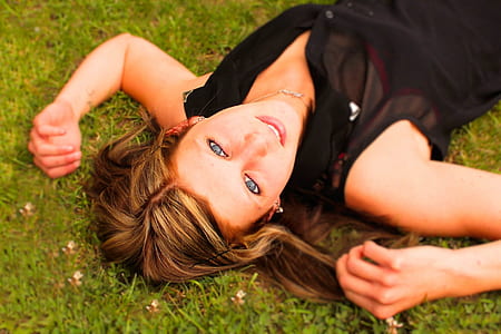 woman in black collared button-up sleeveless top lying on green grass