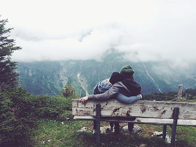 man and woman sit on bench in front of mountain during daytime