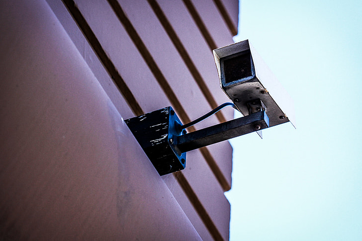 worm's eye view photography of white CCTV camera mounted on brown building during daytime