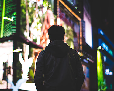 selective focus photography of person in leather jacket during nightime with LED signages background