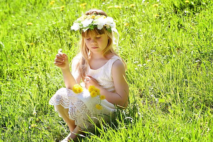 girl wearing white lace dress and flower crown sitting on green grass