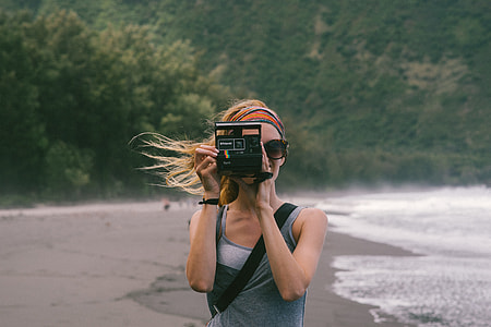 woman taking picture with black land camera in a beach during daytime
