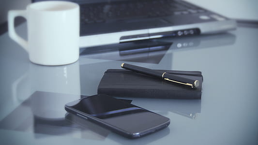 black smartphone near pen and notebook