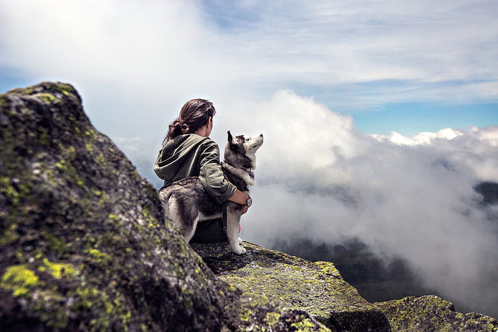 person holding husky sitting on mountain near clouds