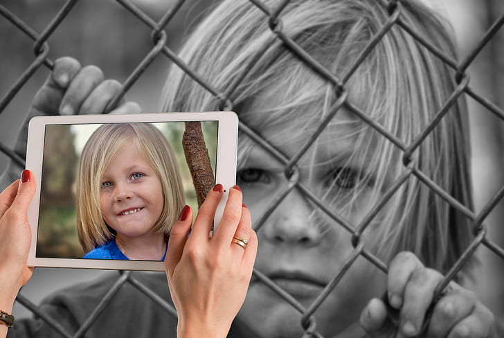 grayscale photograph of boy holding on chain link fence