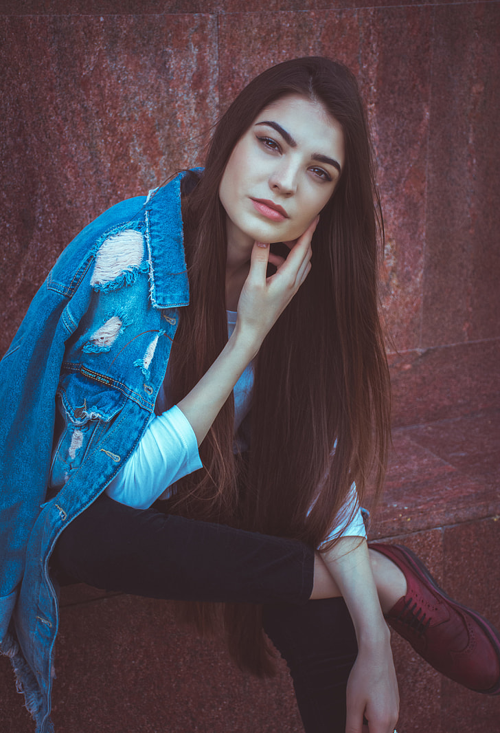 woman with blue denim distressed jacket sitting near red wall