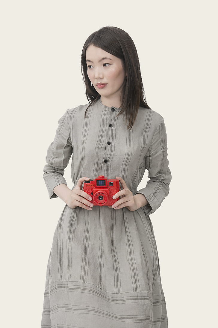 woman in gray dress holding red camera