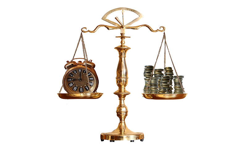 brass-colored balance scale with analog clock and coins