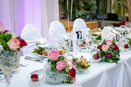 three flower arrangements on top of white table near drinking glasses and plates