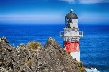 white and red lighthouse near grey rock formation and sea during daytime