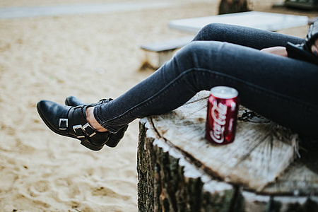 Beautiful blonde woman relaxing with a can of coke on a tree stump by the beach