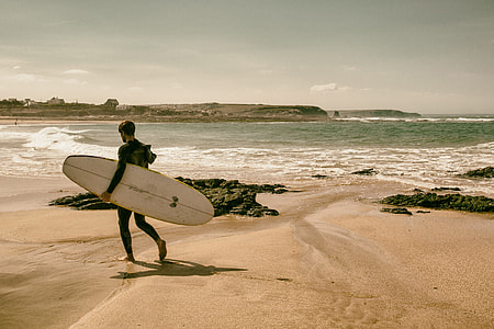 A surfer walks along the beach on the coast of Cornwall, England. Image captured with a Canon 5D DSLR