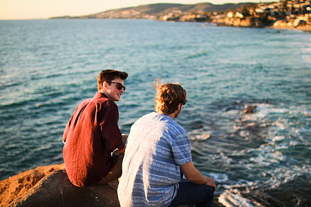 two men sitting on rock by the sea at daytime