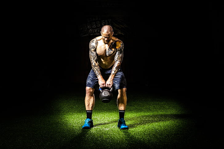 man with tattoos carrying black kettle bell