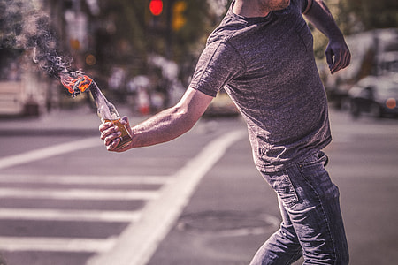 man wearing gray shirt holding burning molotov on street