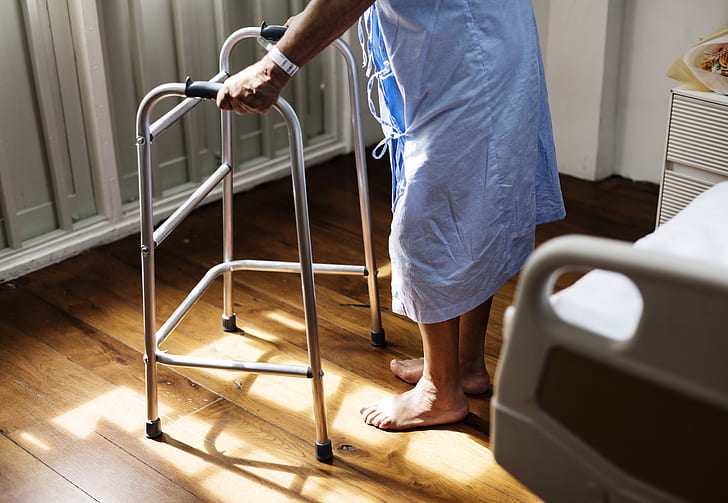 person walks with gray metal folding walker near closed door during daytime