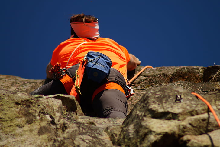 Person in Orange Shirt Climbing Rock during Daytime