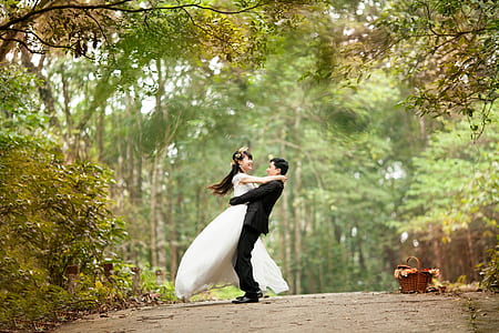 selective focus photo of a groom carrying bride under green tall trees